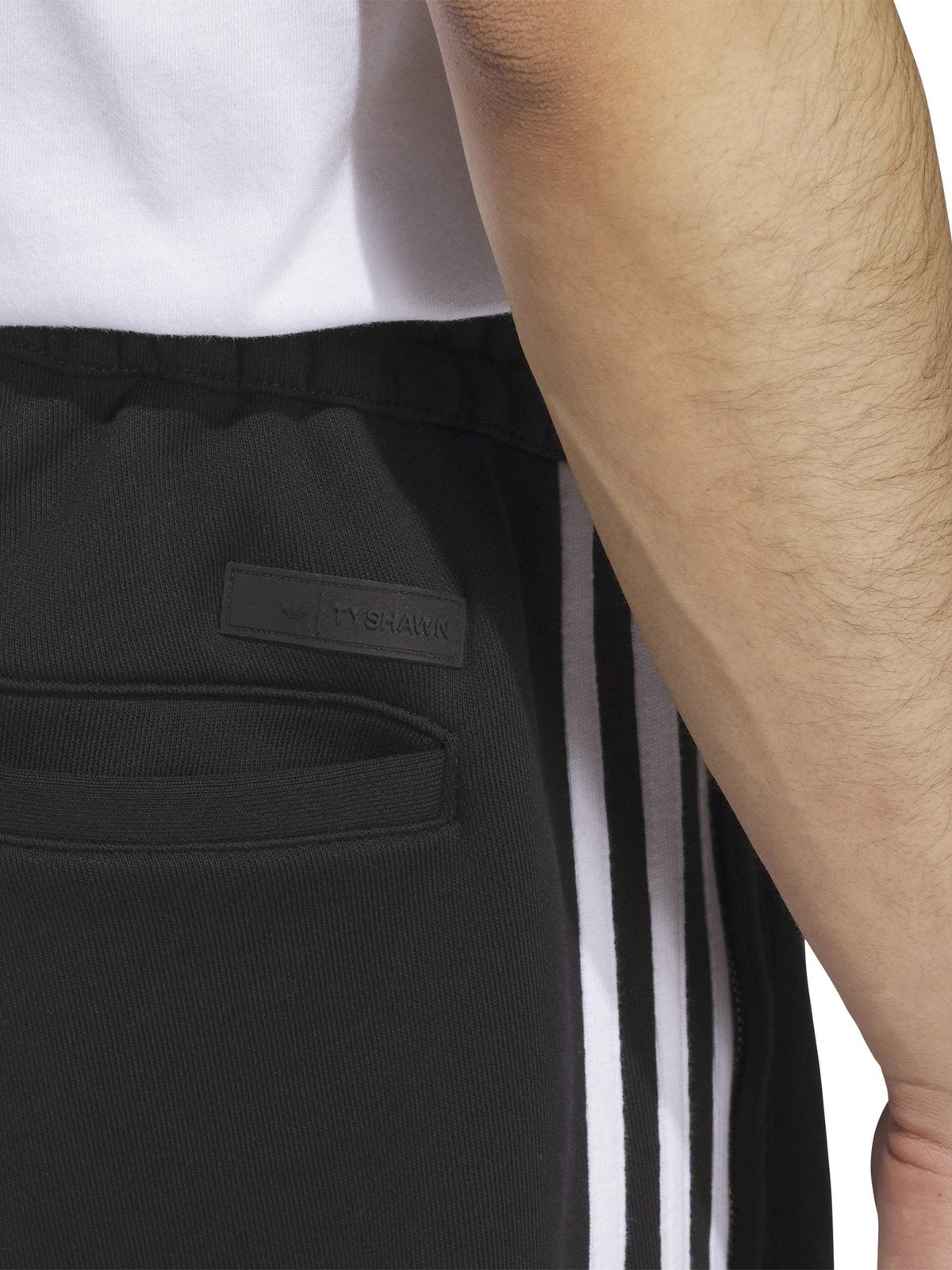 Pantalons Adidas Tysh Trck Pant Black/White, gros plan sur la poche, les trois bandes blanches et le logo trèfle doré